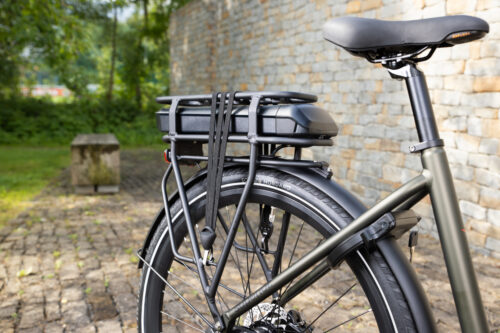 Zijkant van een e-bike met een bagagedrager en accu, vooraanzicht, tegen een stenen muur.